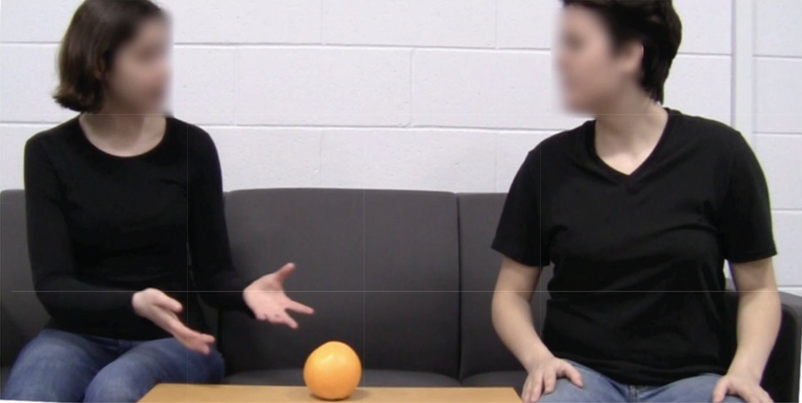 Two people seated on a couch with an orange on the table between them, illustrating the negotiation scenario where both want the orange but for different purposes.